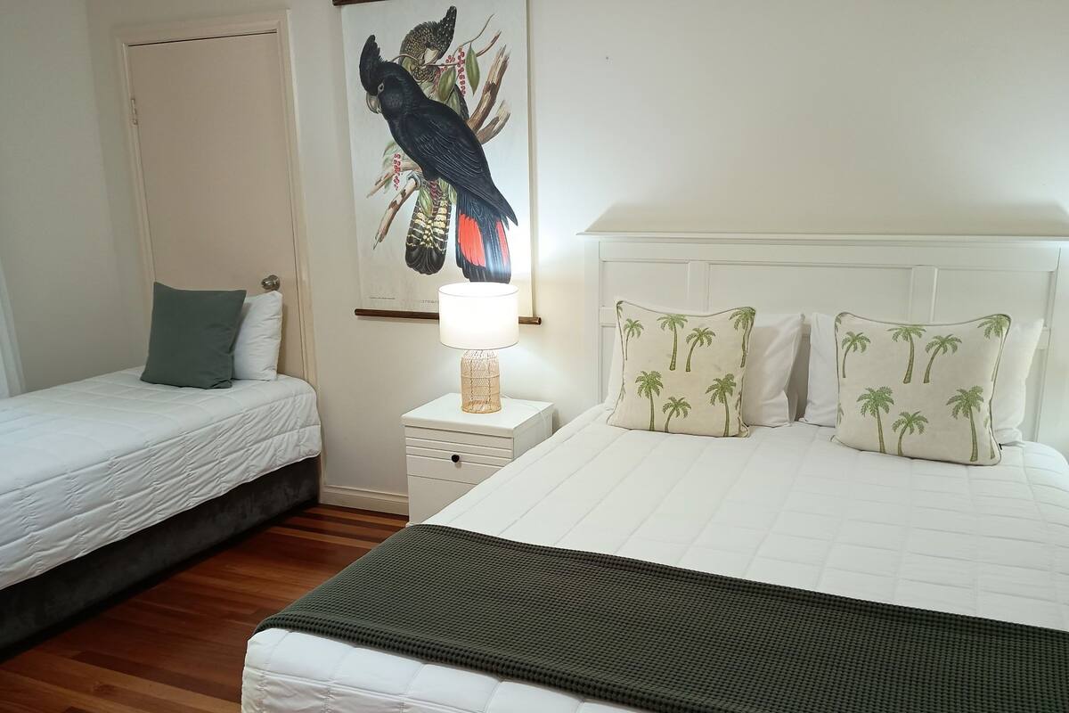 A bedroom with two single beds, a nightstand with a lamp, and a wall-mounted painting of a bird.