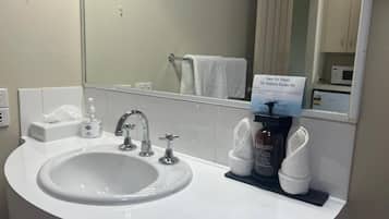 Une salle de bain avec un lavabo blanc, un miroir et un panneau rappelant l’importance de préserver la planète.