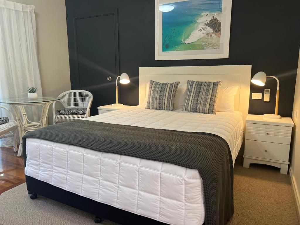 Een slaapkamer met een bed, bedlampen, een nachtkastje, een stoel, een klein tafeltje en een aan de muur hangend schilderij.