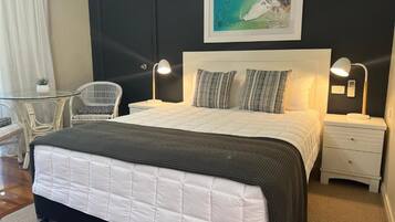 Een slaapkamer met een bed, bedlampen, een nachtkastje, een stoel, een klein tafeltje en een aan de muur hangend schilderij.