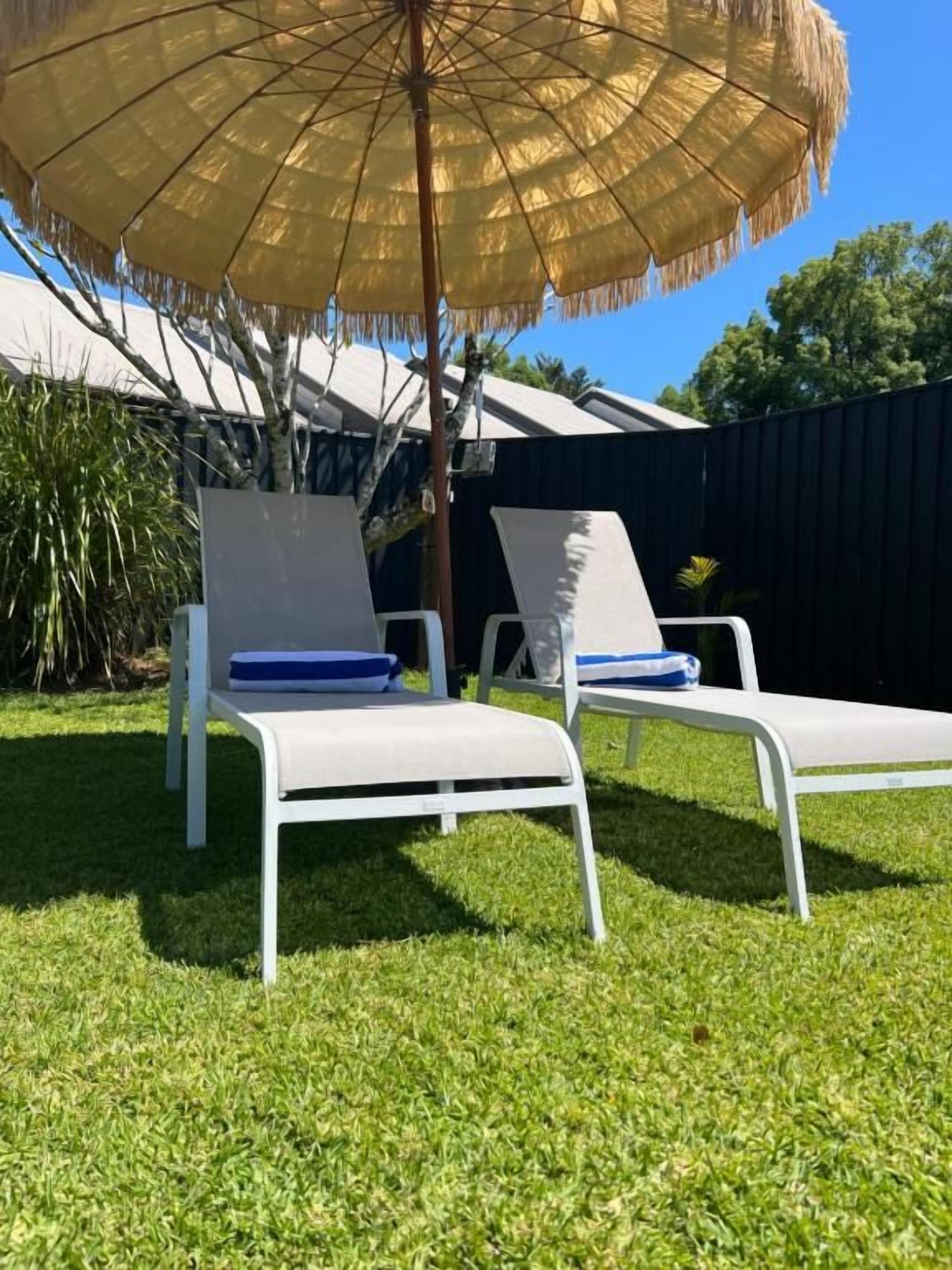 Dues cadires relaxants amb coixins blaus, un parasol de palla i un jardí ben cuidat.