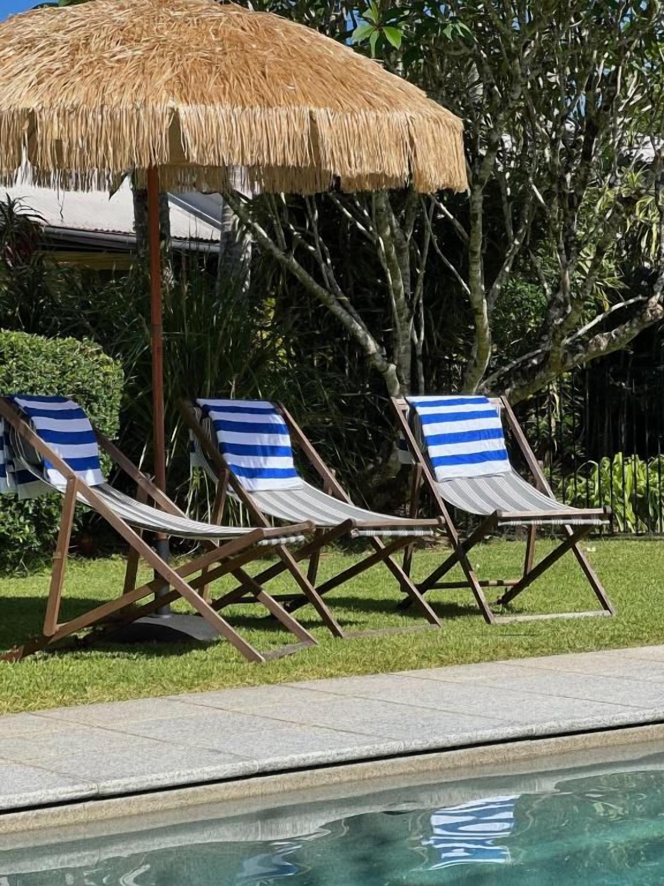 A poolside area with lounge chairs and a thatched umbrella.