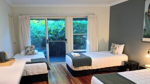 A hotel room with two beds, a sliding glass door to a garden, a small table with a kettle, and a nightstand with a lamp. - Arabella Garden Inn Motel (Wollongbar)