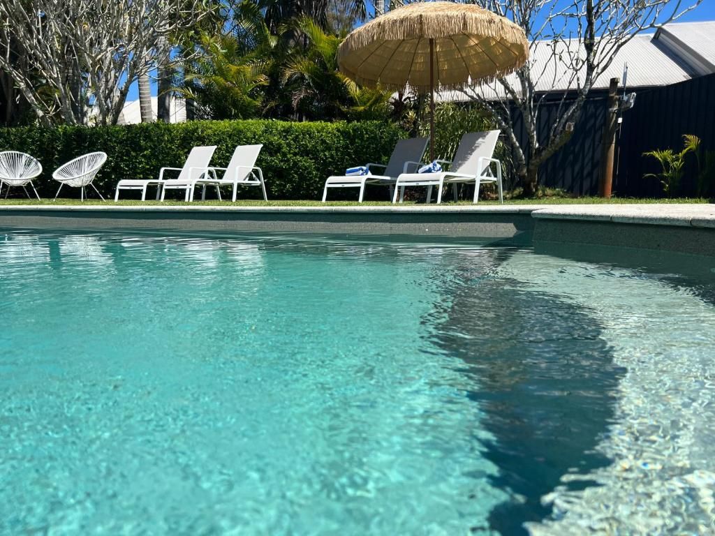 A clear swimming pool with lounge chairs and a thatched umbrella.