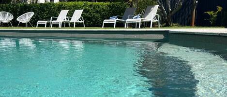A clear swimming pool with lounge chairs and a thatched umbrella.