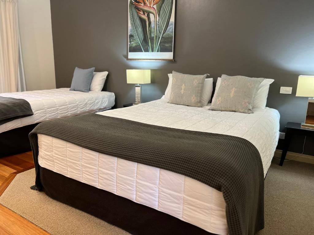 A hotel room with two beds, a large bed with a dark headboard and a smaller bed with a white headboard, both with matching pillows and a large painting on the wall.