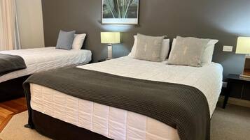 Habitación de hotel con dos camas, una cama grande con cabecera oscura y una cama más pequeña con cabecera blanca, ambas con almohadas a juego y un cuadro grande en la pared.