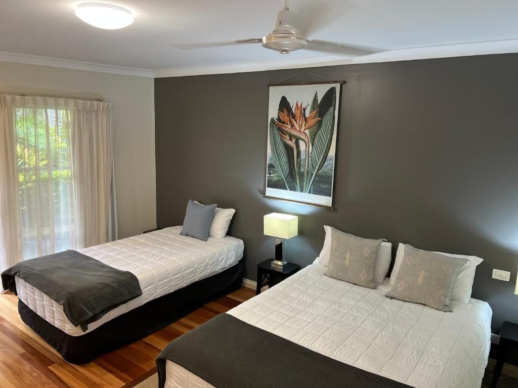 A hotel room with two beds, a ceiling fan, a window with curtains, and a wall-mounted painting.
