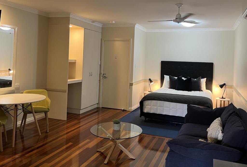 A hotel room with a bed, a round glass table, a sofa, a ceiling fan, and a door leading to a bathroom.
