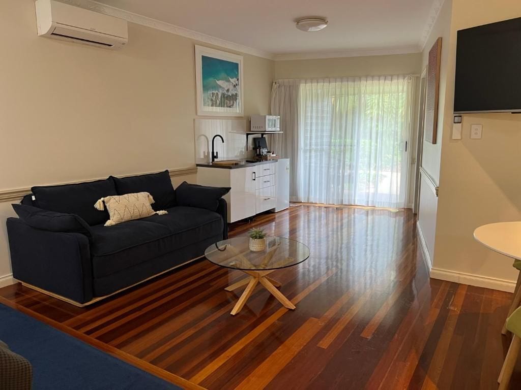 A living room with a sofa, a glass coffee table, and a kitchen area with a sink and cabinets.