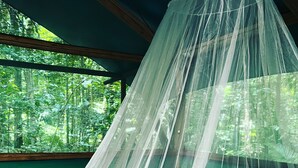 A bed with a white canopy and a view of a forest through a window. - Daintree Crocodylus (Cow Bay)