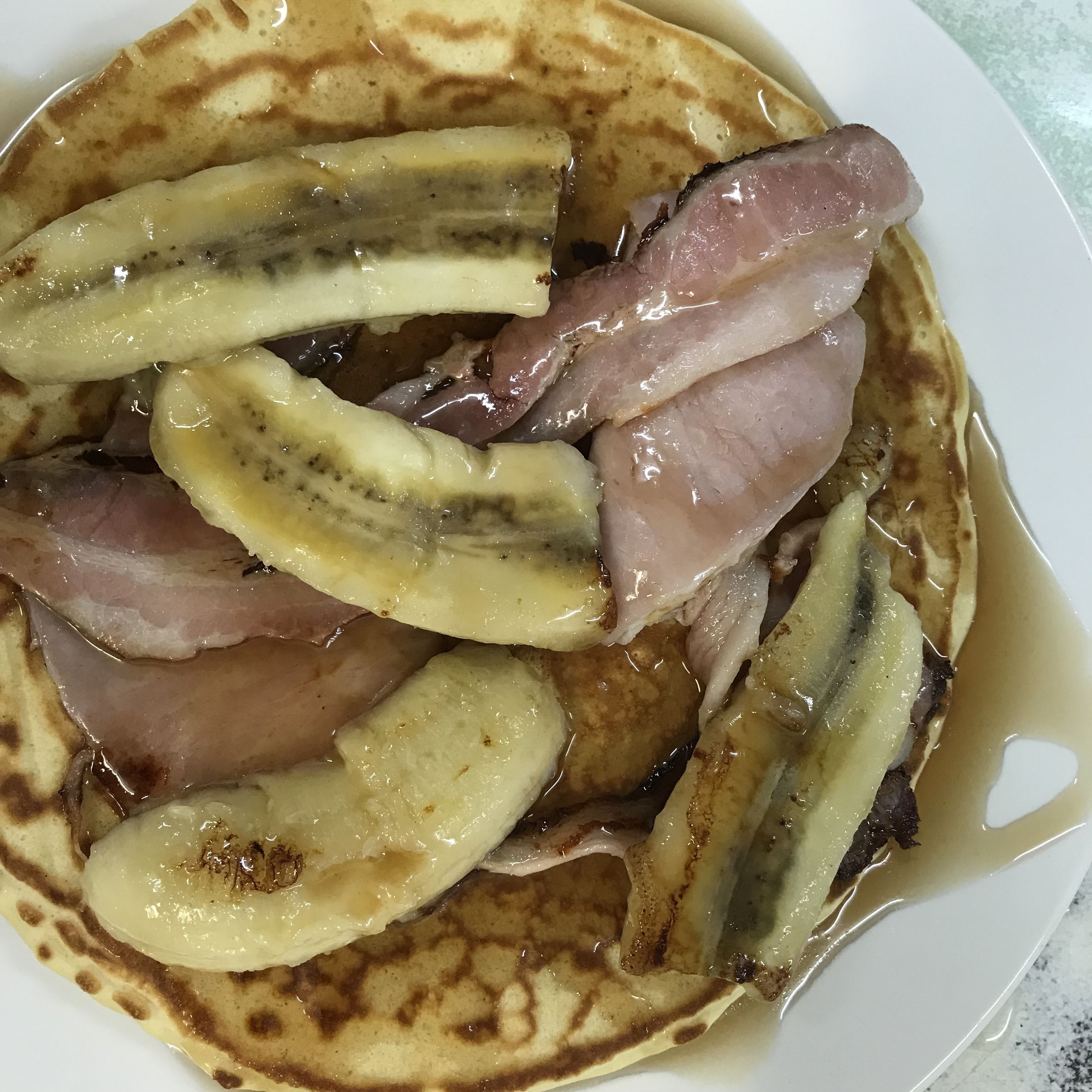 A plate of pancakes with banana slices and bacon.