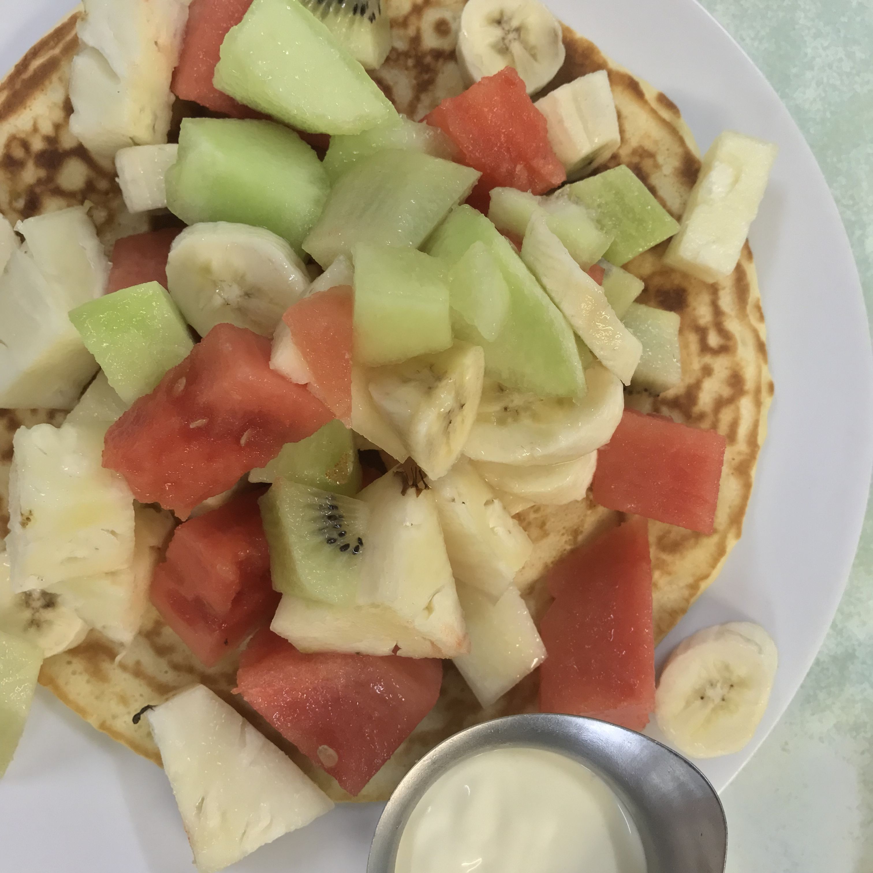 A plate of fruit-topped pancakes with a small bowl of sauce.