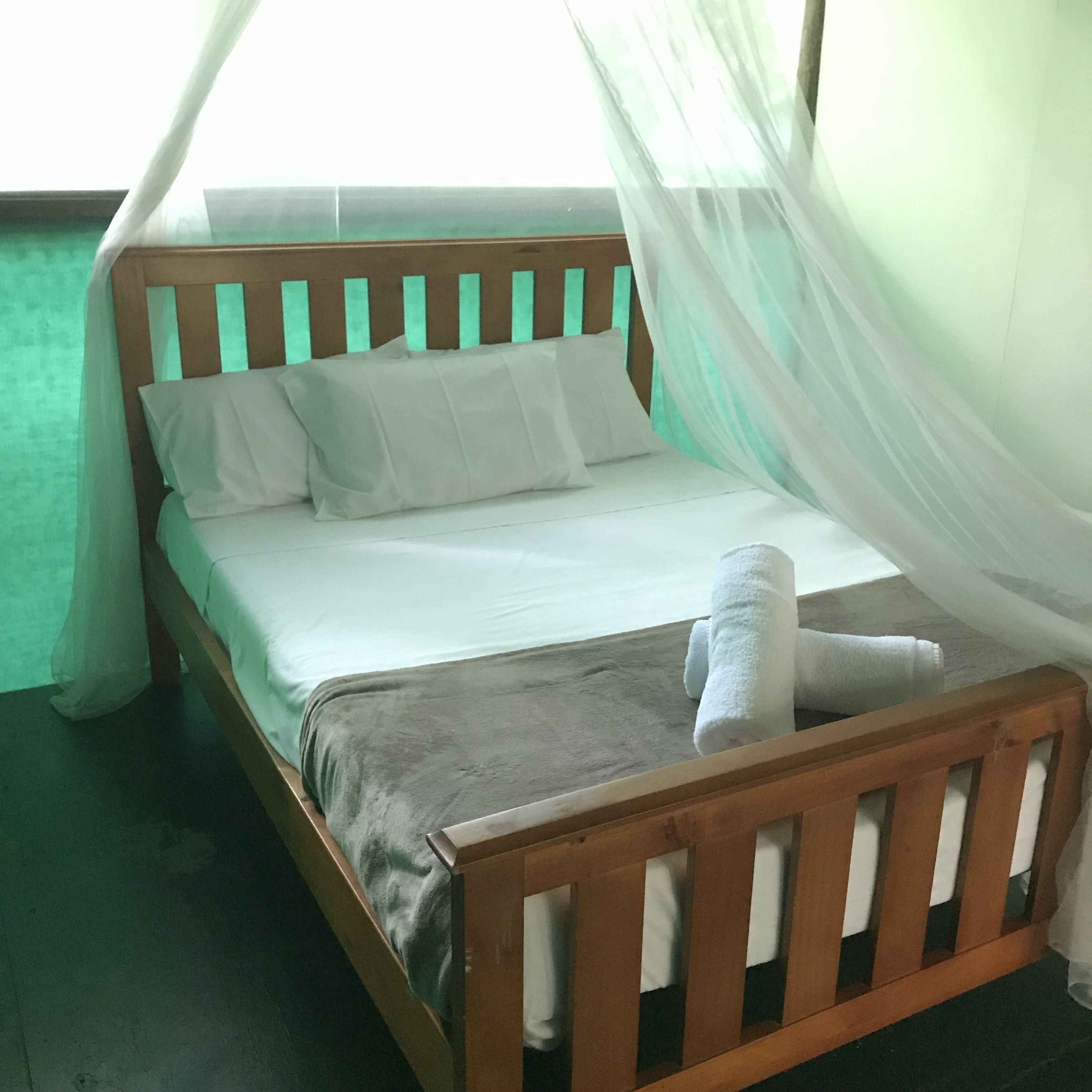 A bed with a wooden frame, white bedding, and a grey blanket.