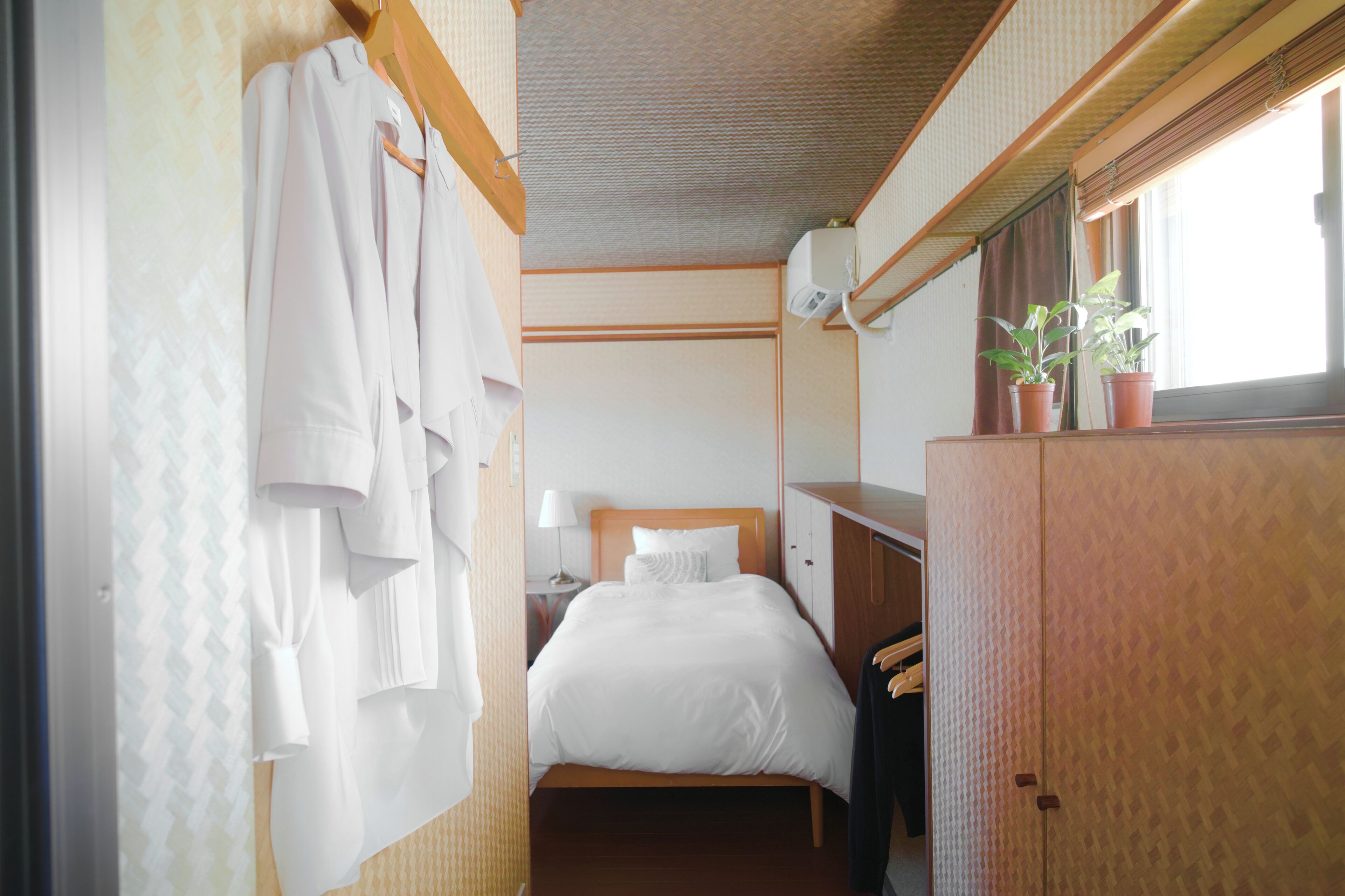 Una habitación de hotel con cama, armario, escritorio y ventana con plantas.