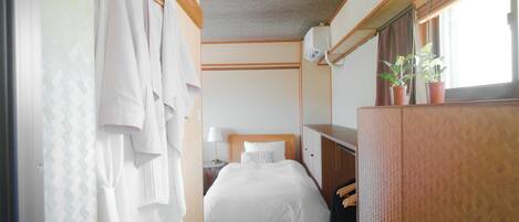 Una habitación de hotel con cama, armario, escritorio y ventana con plantas.
