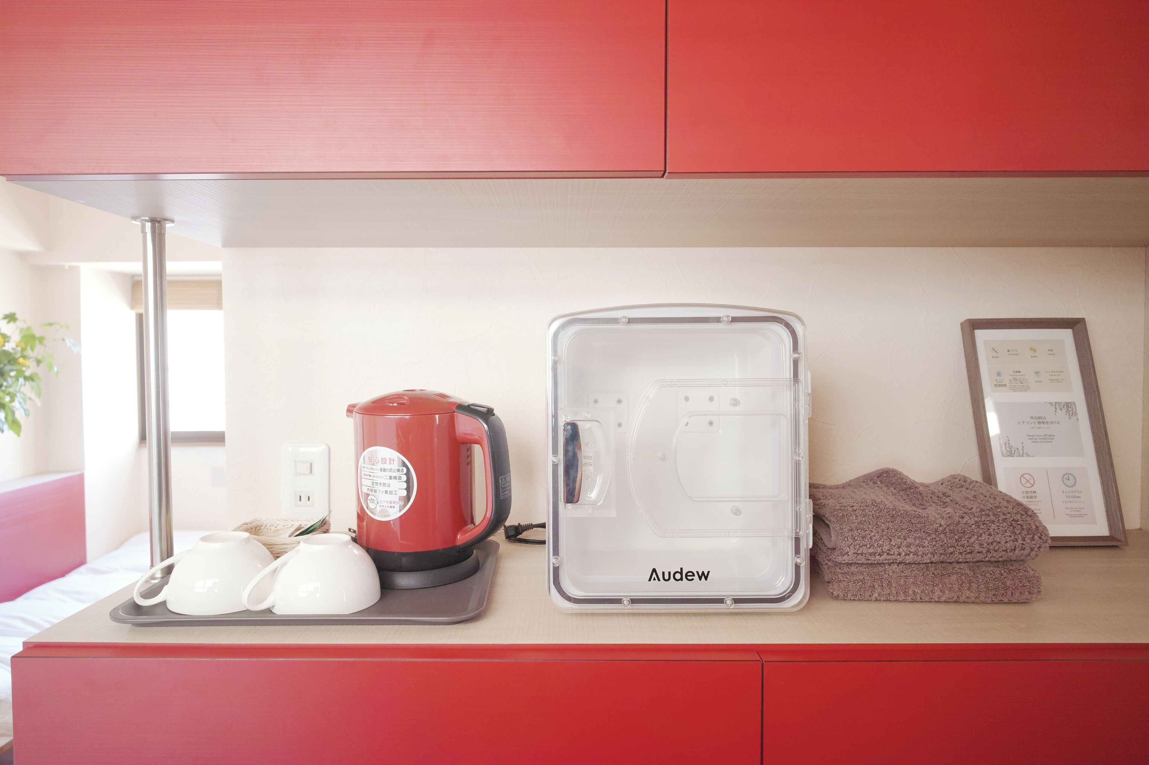 A kitchenette with a red coffee maker, a transparent water dispenser, and a framed menu on the counter.