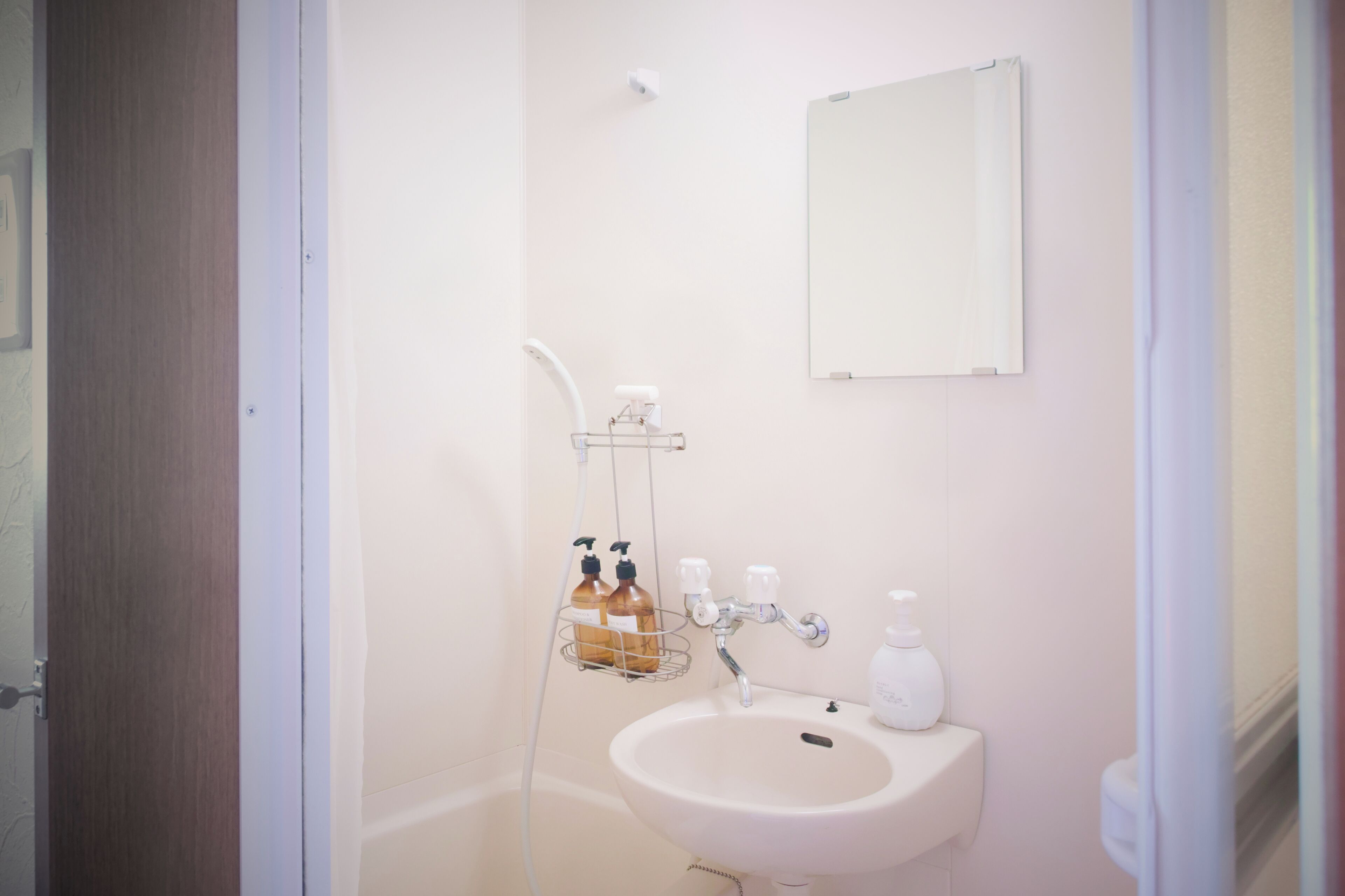 Un baño con lavamanos blanco, un espejo y zona de ducha.