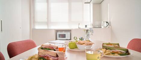A dining table with sandwiches, apples, and a cup of tea in a bright room with a window and a microwave in the background.
