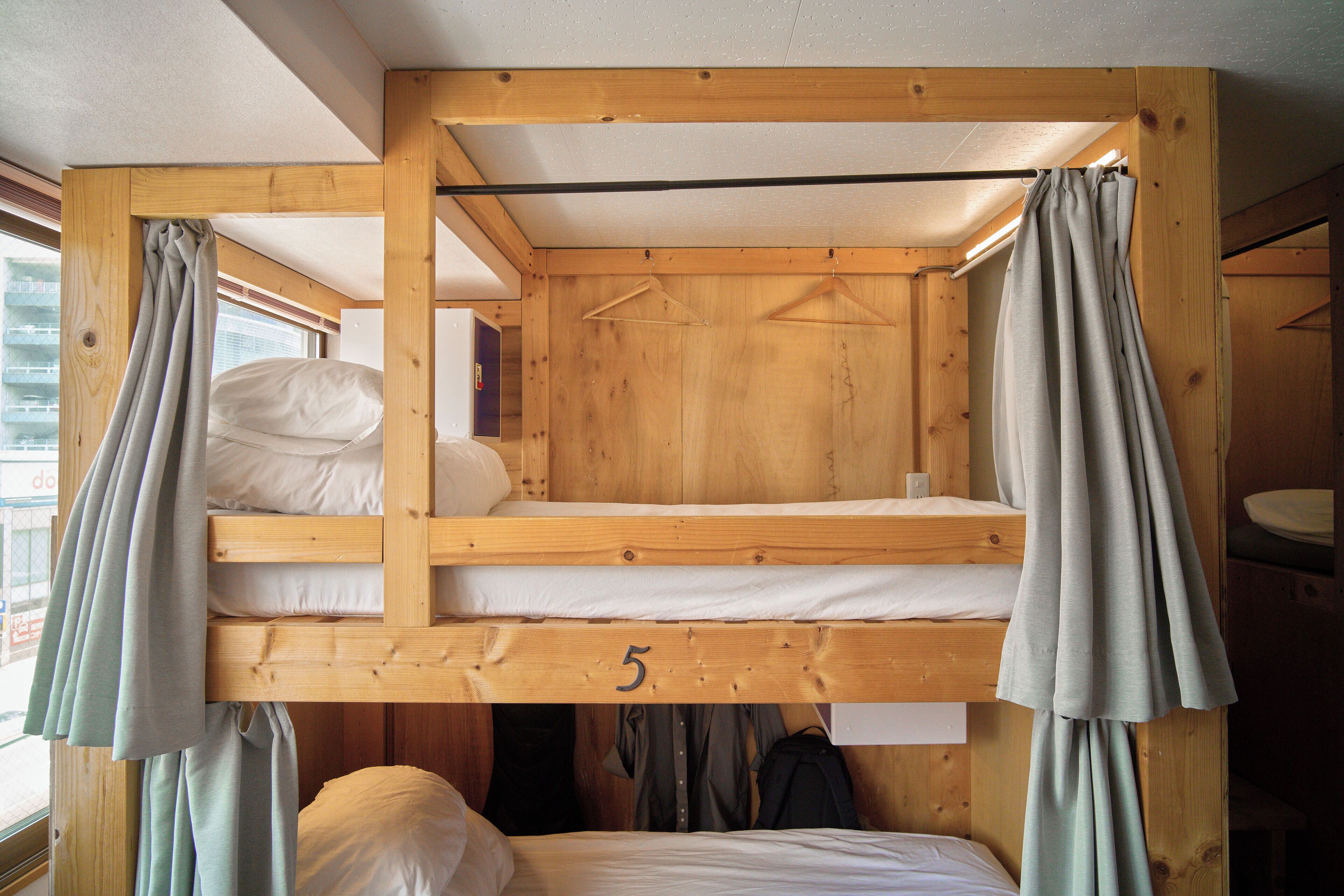 Habitación con literas de madera, el camarote inferior marcado con el número 5 y una ventana con cortinas.