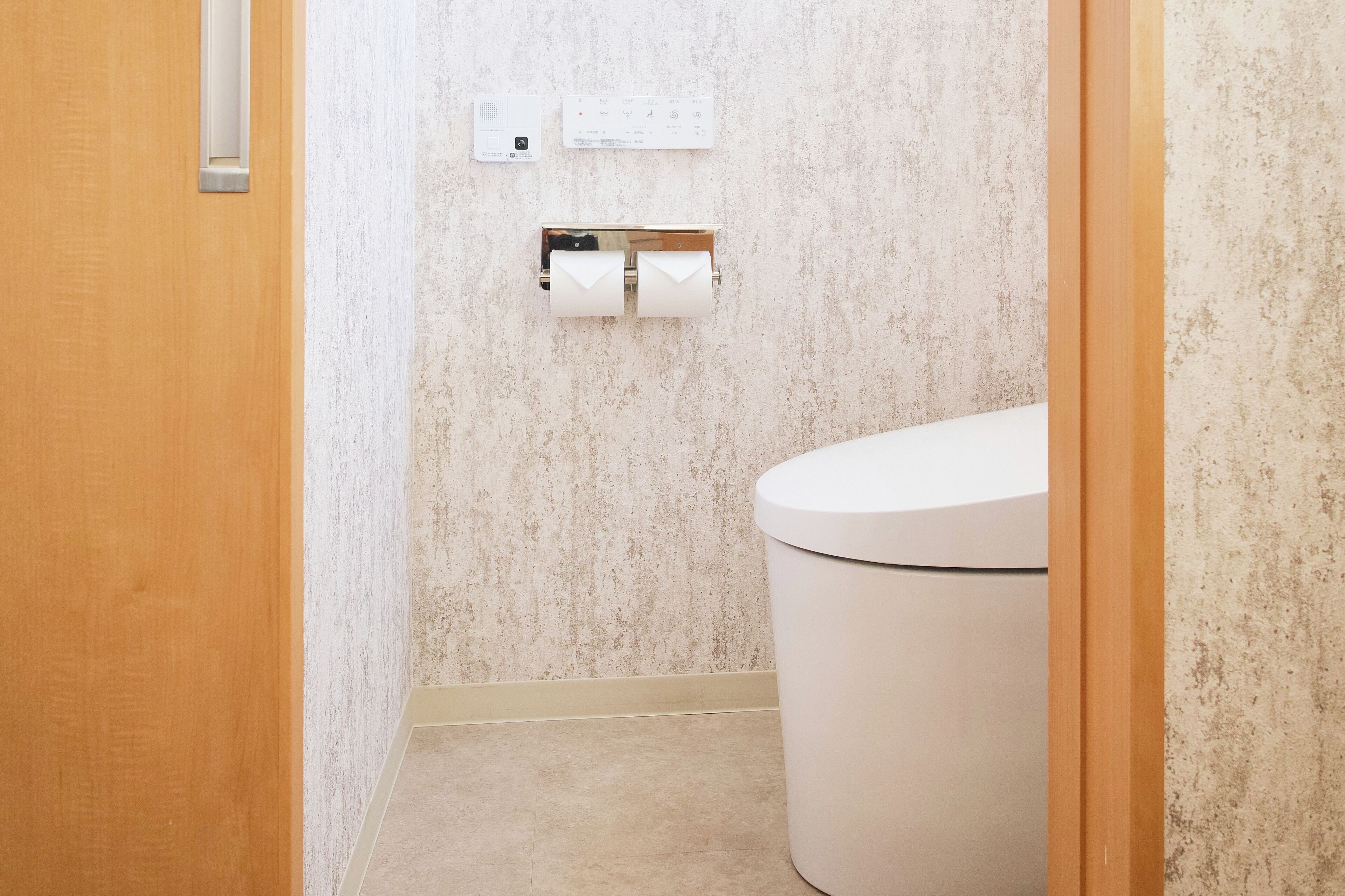 A bathroom with a toilet, a wall-mounted paper towel dispenser, and a thermostat.