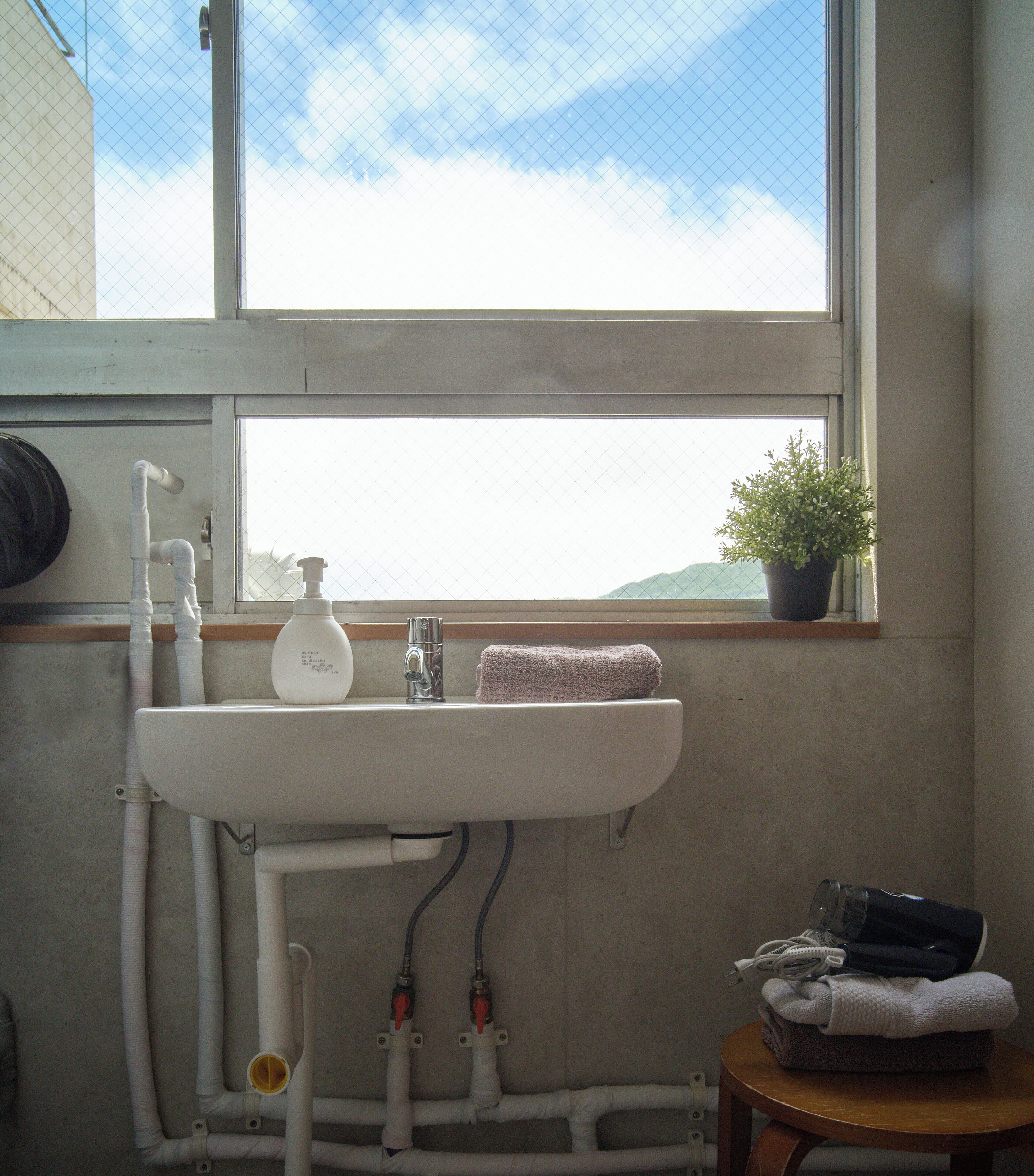 A bathroom with a window, a sink, a towel, a potted plant, and a small table with towels.
