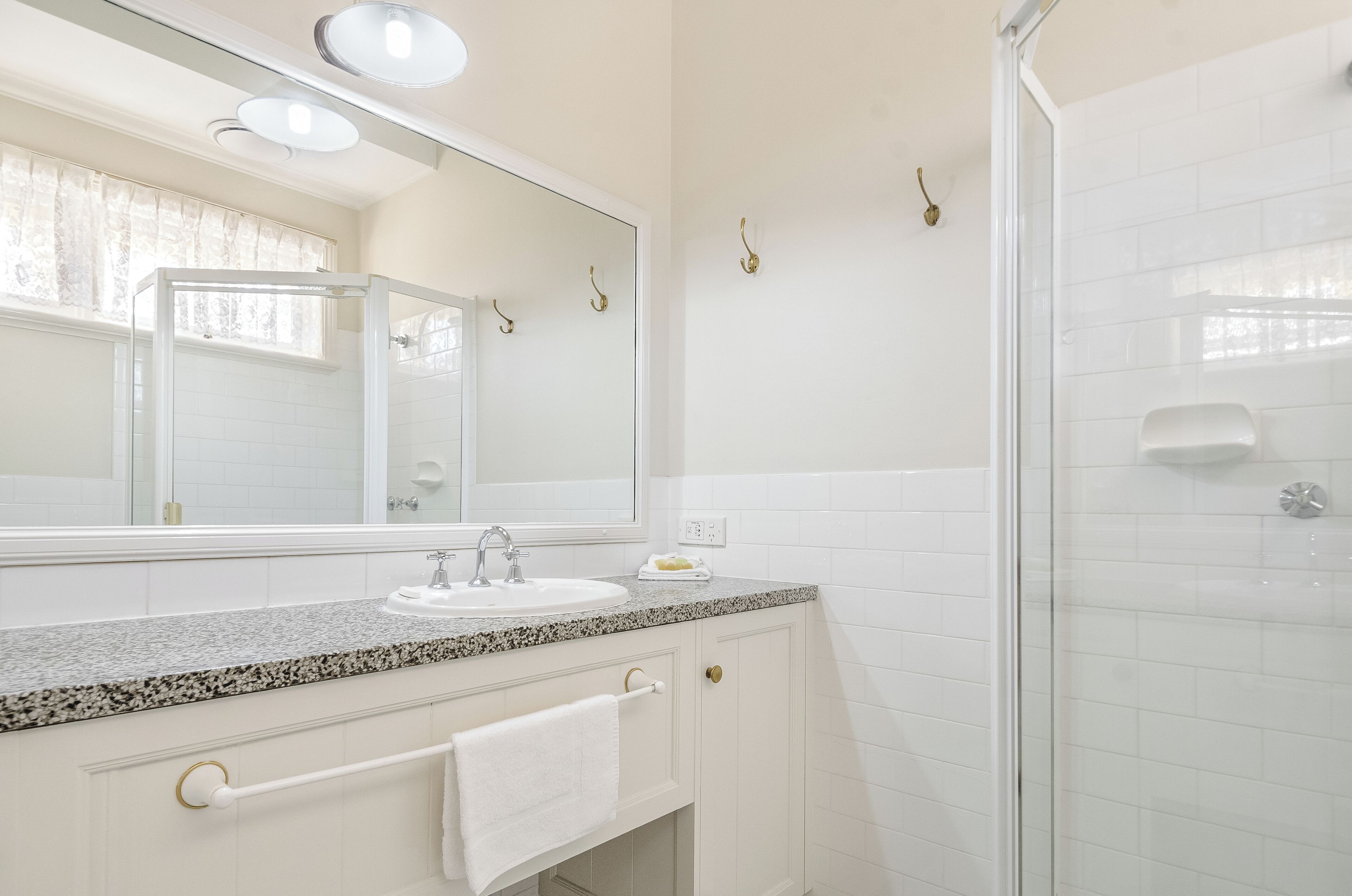 A bathroom with a granite countertop sink, a large mirror, a towel rack, and a glass shower enclosure.