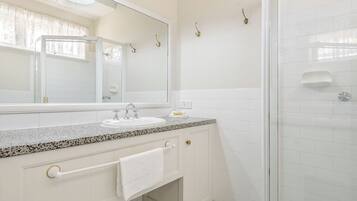 A bathroom with a granite countertop sink, a large mirror, a towel rack, and a glass shower enclosure.