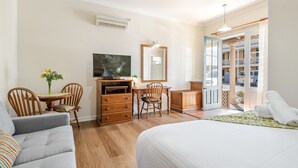 A hotel room with a bed, a desk with a chair, a dresser, a dining table with chairs, a painting, and a view of the outside. - Ballina Heritage Inn (Ballina)