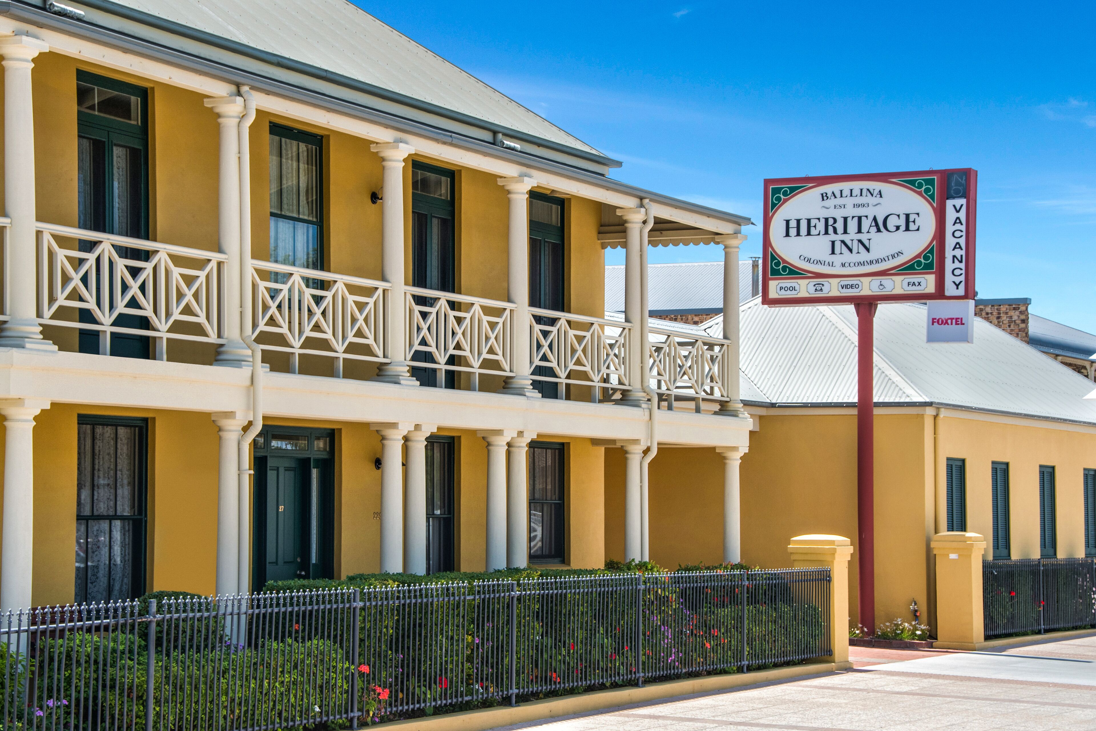A two-story building with a yellow facade, a balcony with white railings, and a sign for the Ballina Heritage Inn.