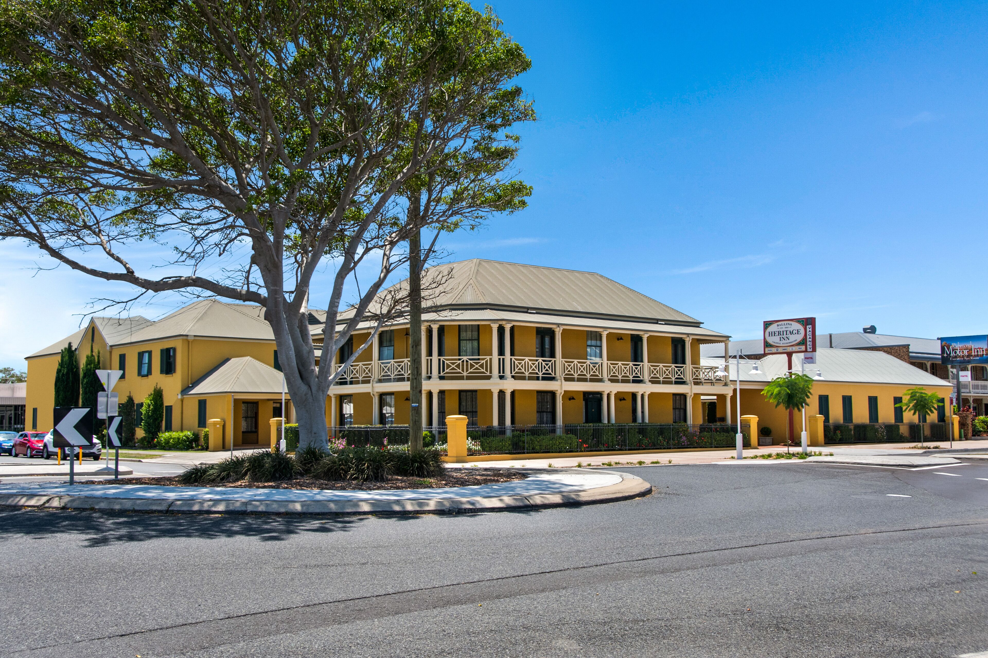 A yellow building with a balcony, a sign for 'Heritage Inn', and a tree in front.