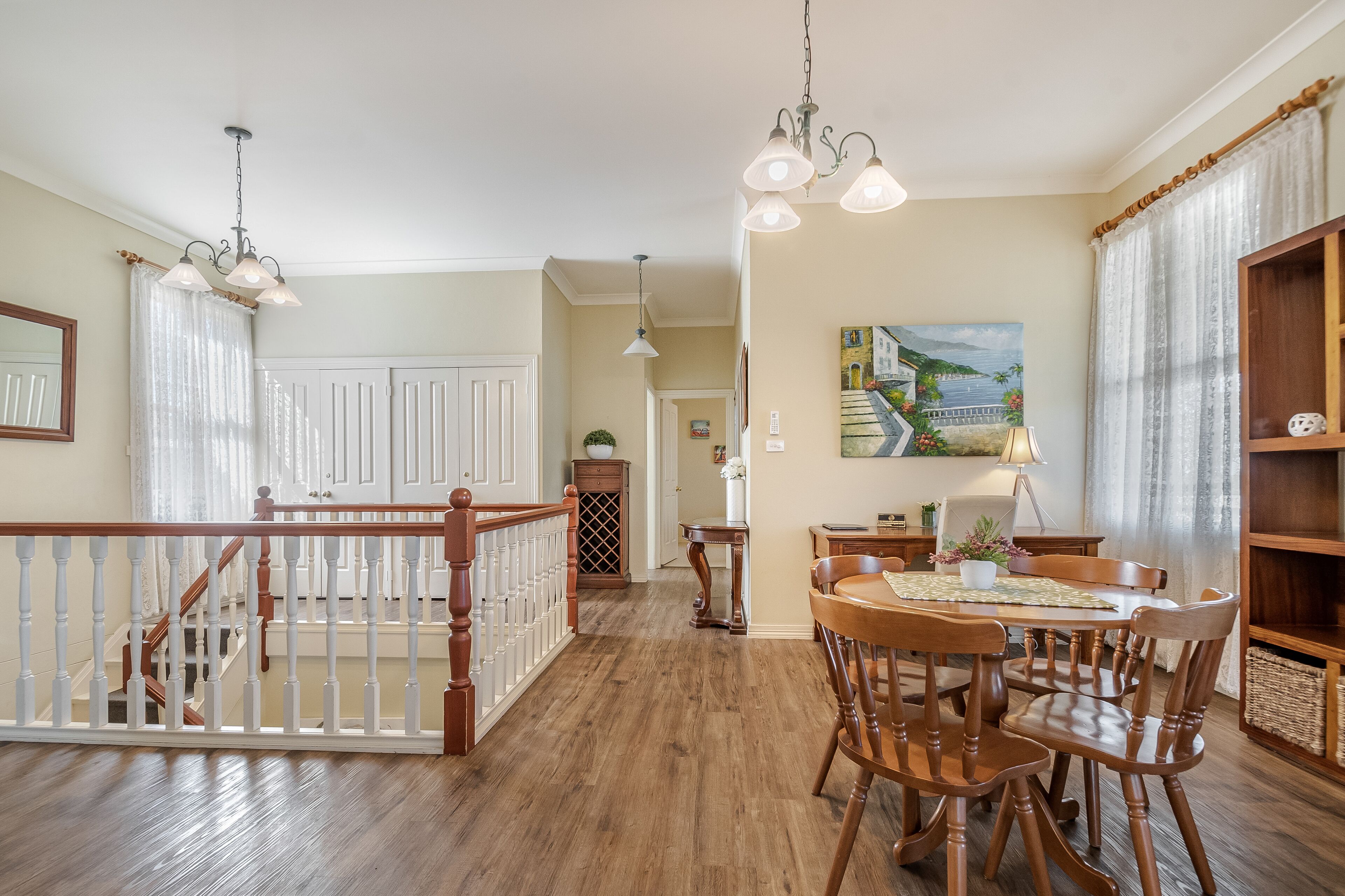 A spacious dining area with wooden chairs and a table, a staircase with a railing, and a painting on the wall.
