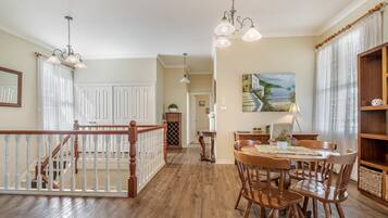 A spacious dining area with wooden chairs and a table, a staircase with a railing, and a painting on the wall.