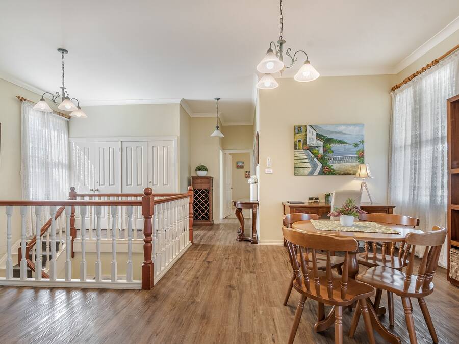 A spacious dining area with wooden chairs and a table, a staircase with a railing, and a painting on the wall.