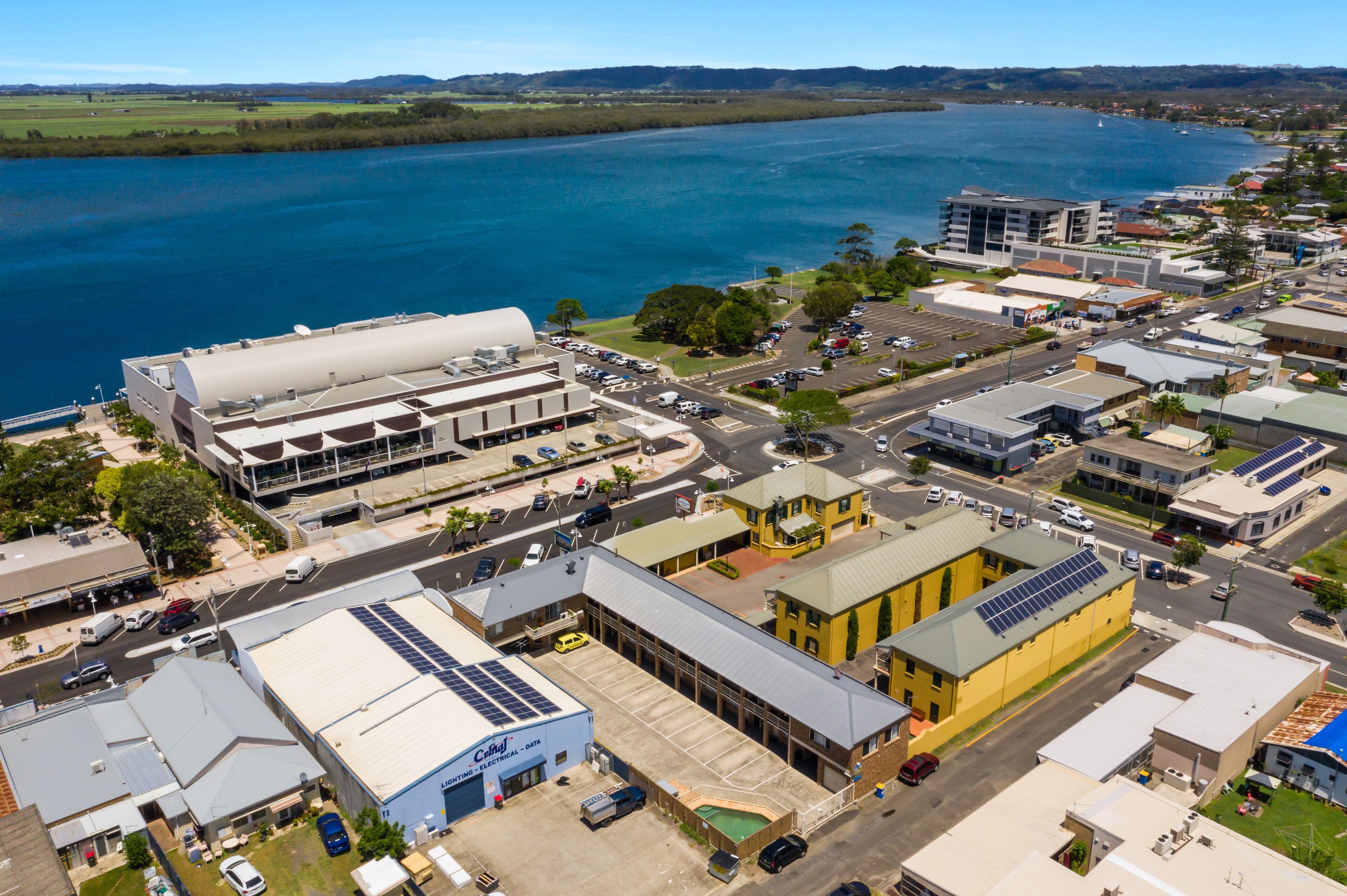 An aerial view of a coastal town with a marina, commercial buildings, and a prominent hotel with a large parking lot.
