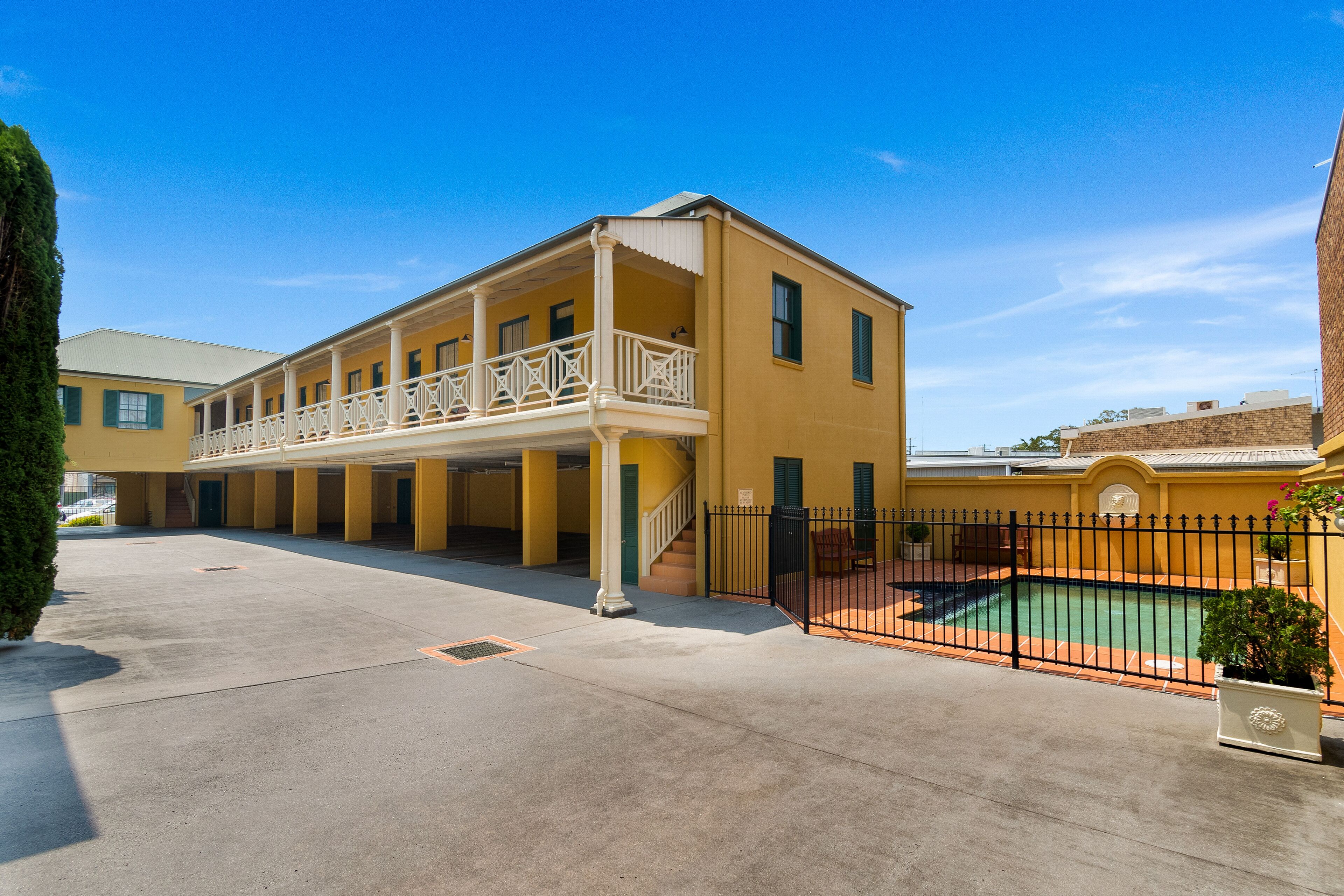 A yellow building with a covered patio and a swimming pool.