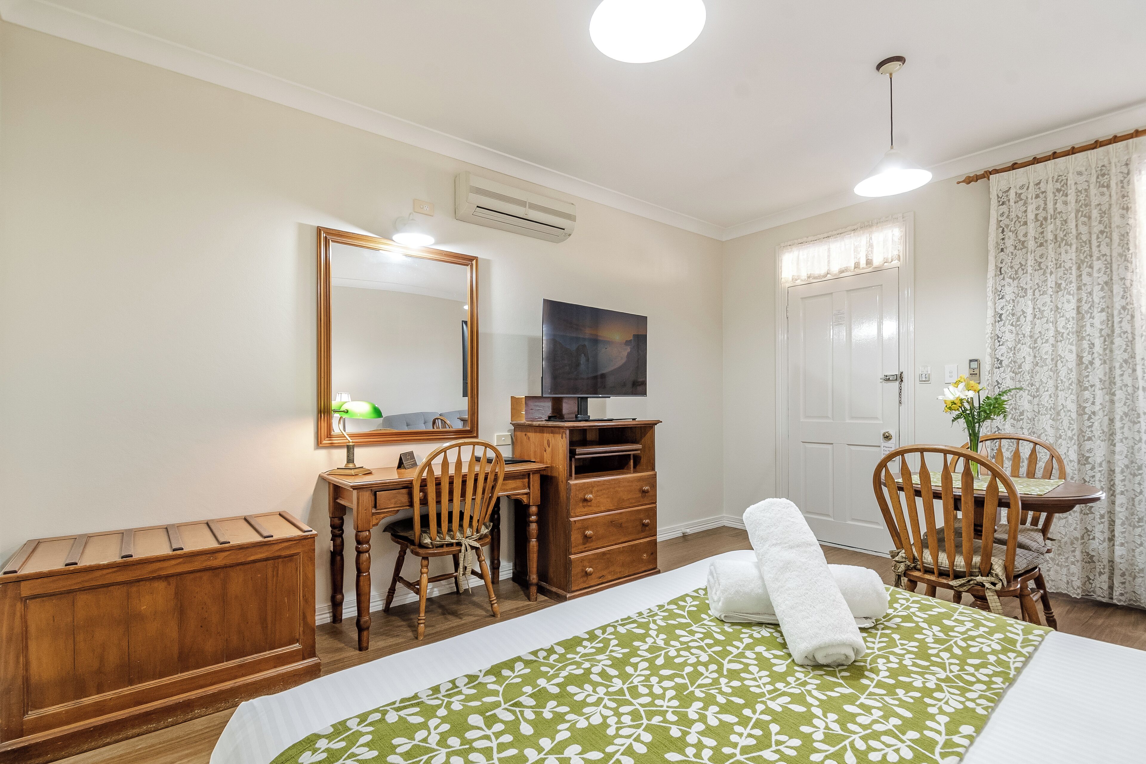 A bedroom with a bed, a desk, a chair, a dresser, and a television.