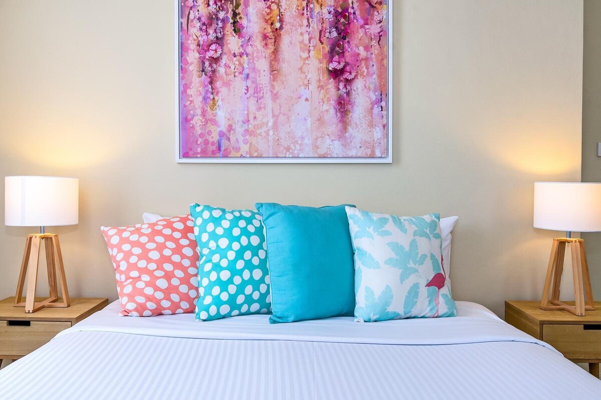 A hotel room with a bed, four pillows, two bedside tables, and a large abstract painting on the wall.