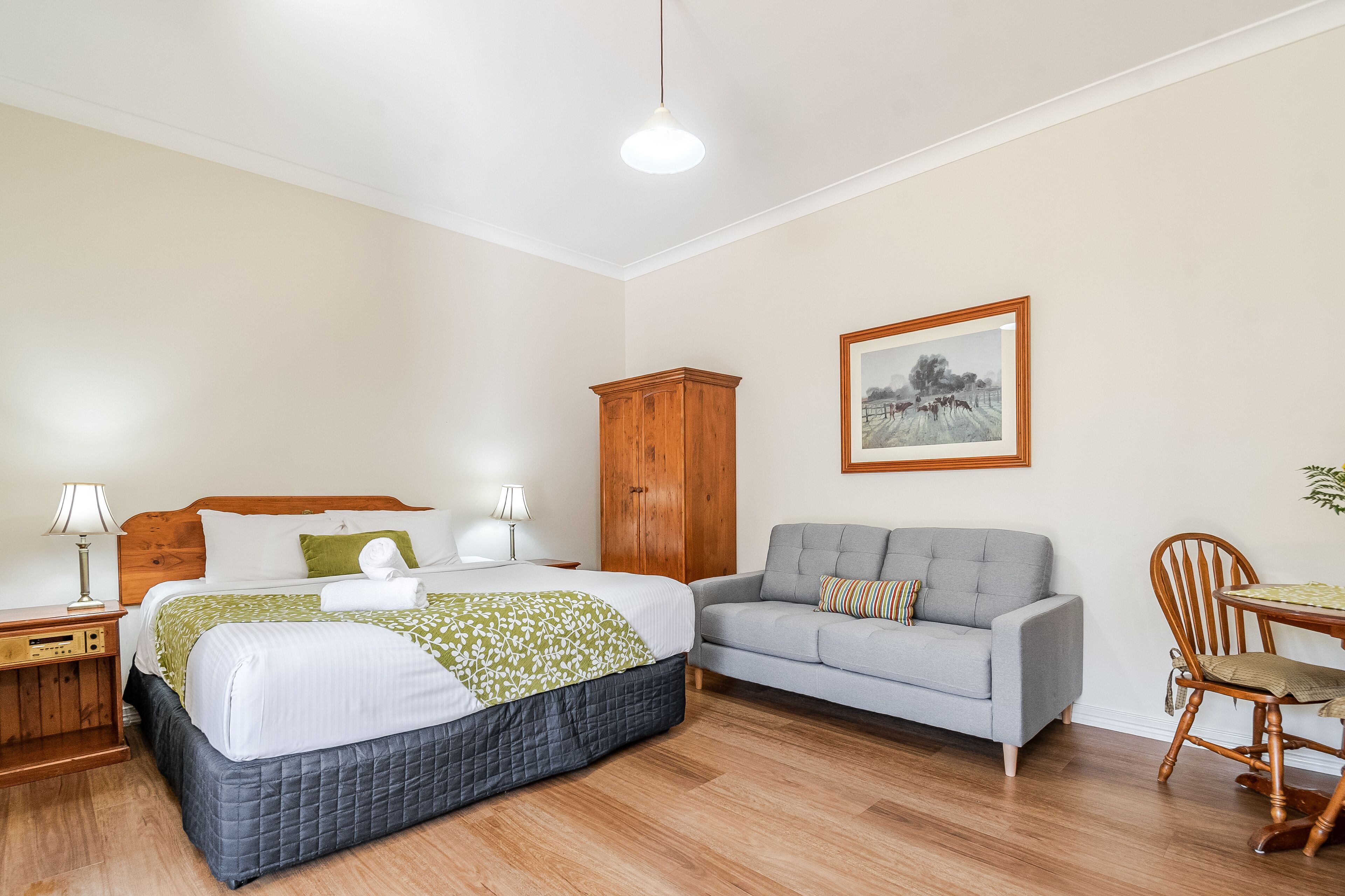 A bedroom with a bed, a grey sofa, a wooden cabinet, and a framed picture on the wall.
