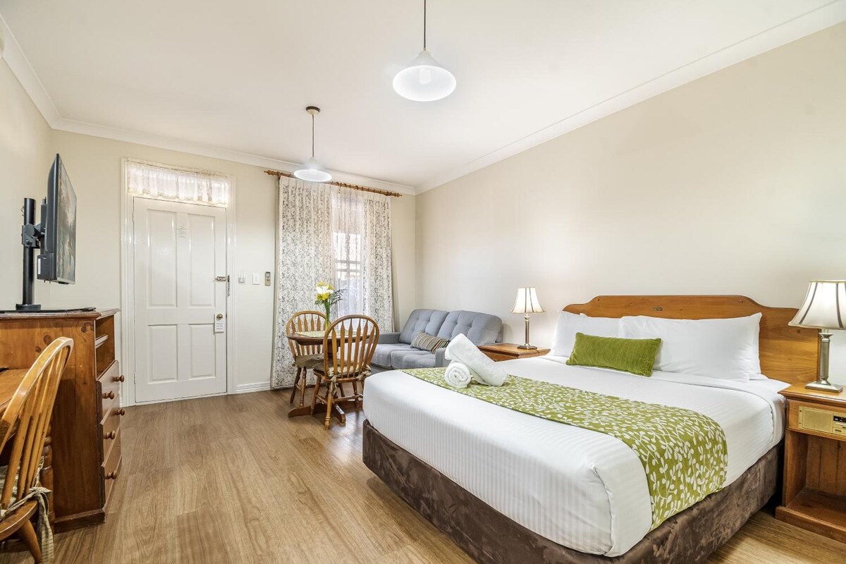 A hotel room with a bed, a desk, a chair, a sofa, and a lamp.