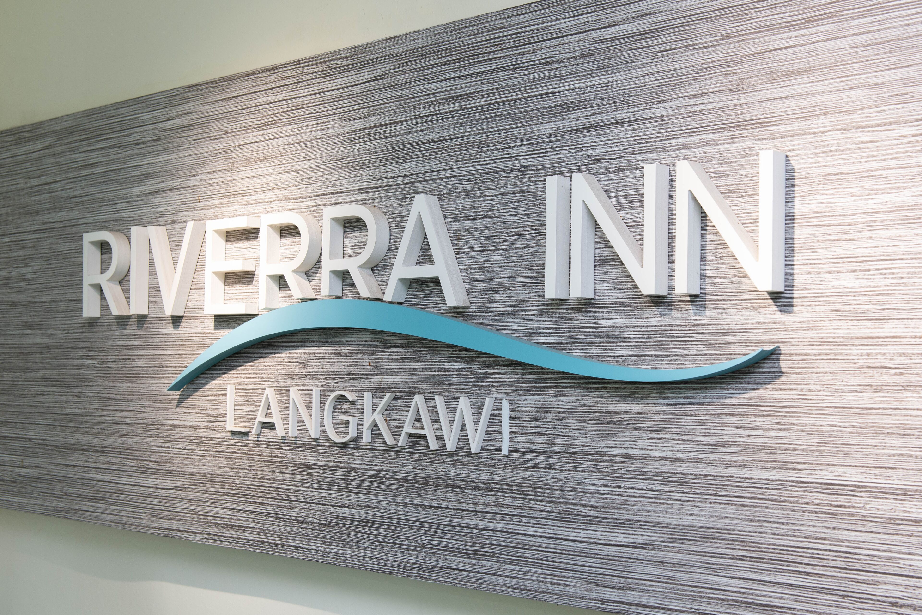 A sign for Riverra Inn Langkawi with a wooden texture background and a stylized wave design.