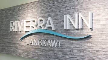 A sign for Riverra Inn Langkawi with a wooden texture background and a stylized wave design.