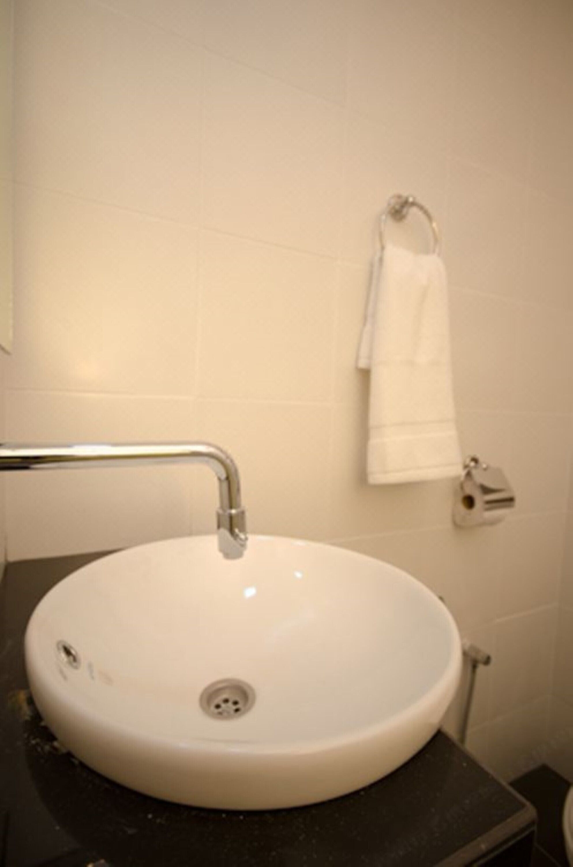 A white bathroom sink with a chrome faucet, a towel hanging on a rack, and a toilet visible in the background.