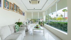 A bright living room with a sofa, a coffee table with plants, large windows, and framed pictures on the wall. - Riverra Inn Langkawi (Langkawi)