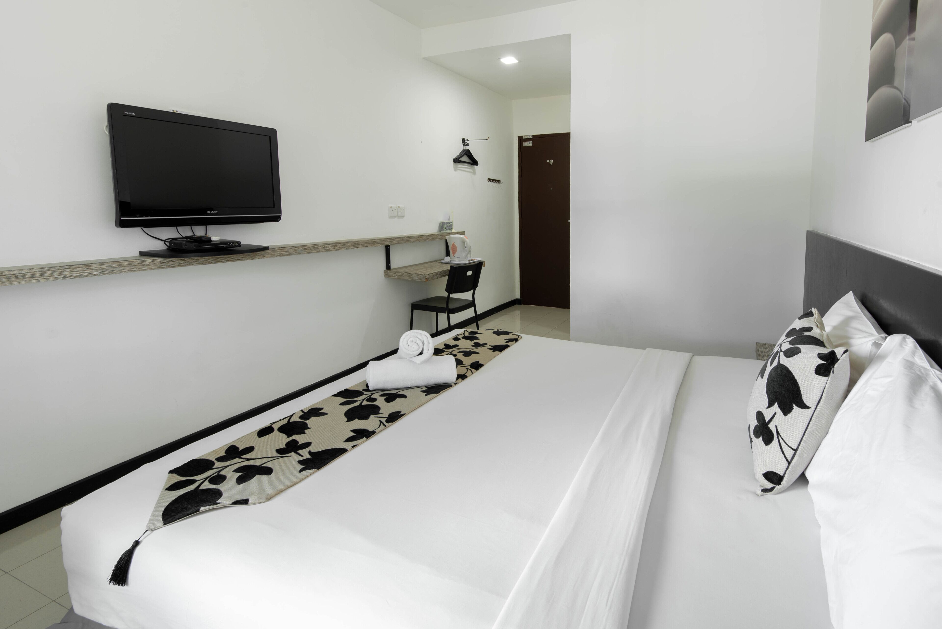 A hotel room with a bed, a TV mounted on the wall, a desk with a chair, and a door.