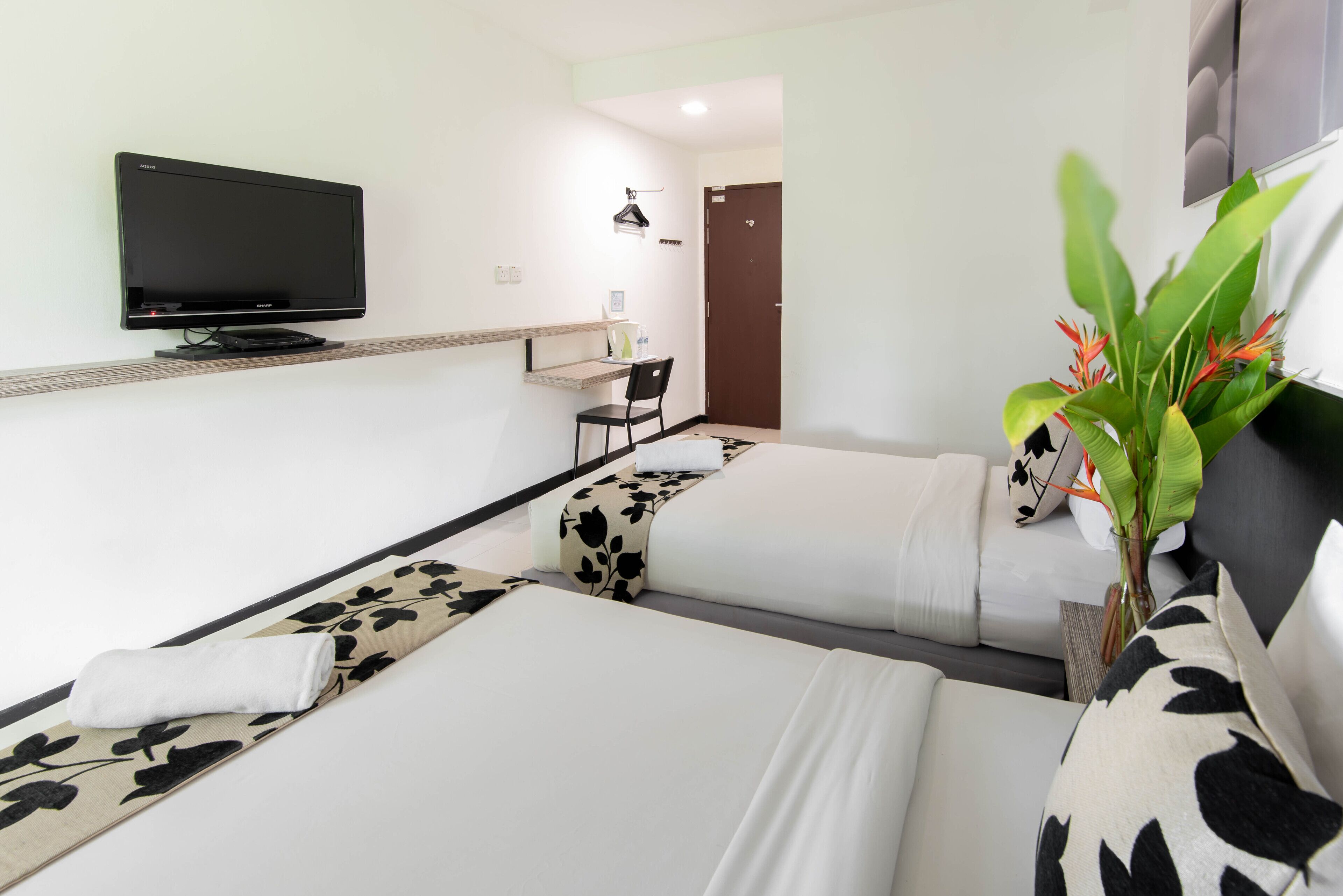 A hotel room with two beds, a flat-screen TV mounted on the wall, a desk, and a chair.