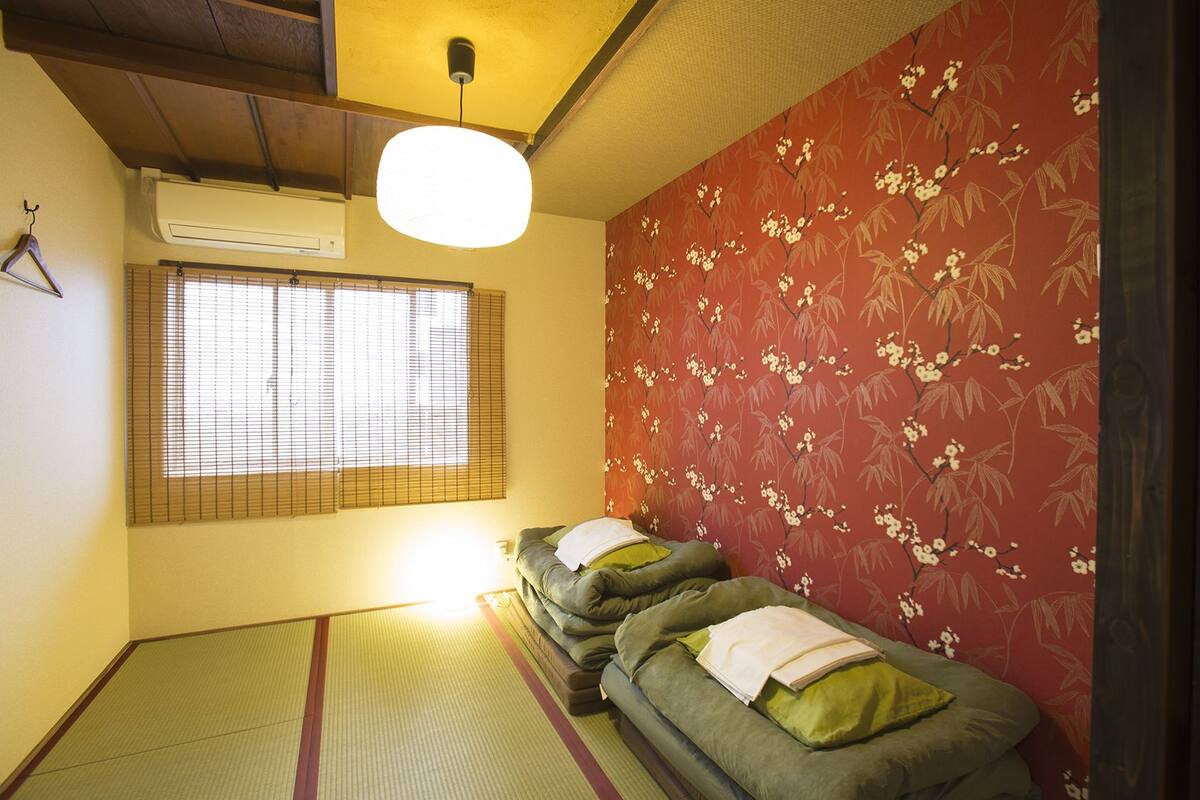 Una habitación japonesa tradicional con suelo de tatami, futón, puertas correderas shoji y papel tapiz floral.