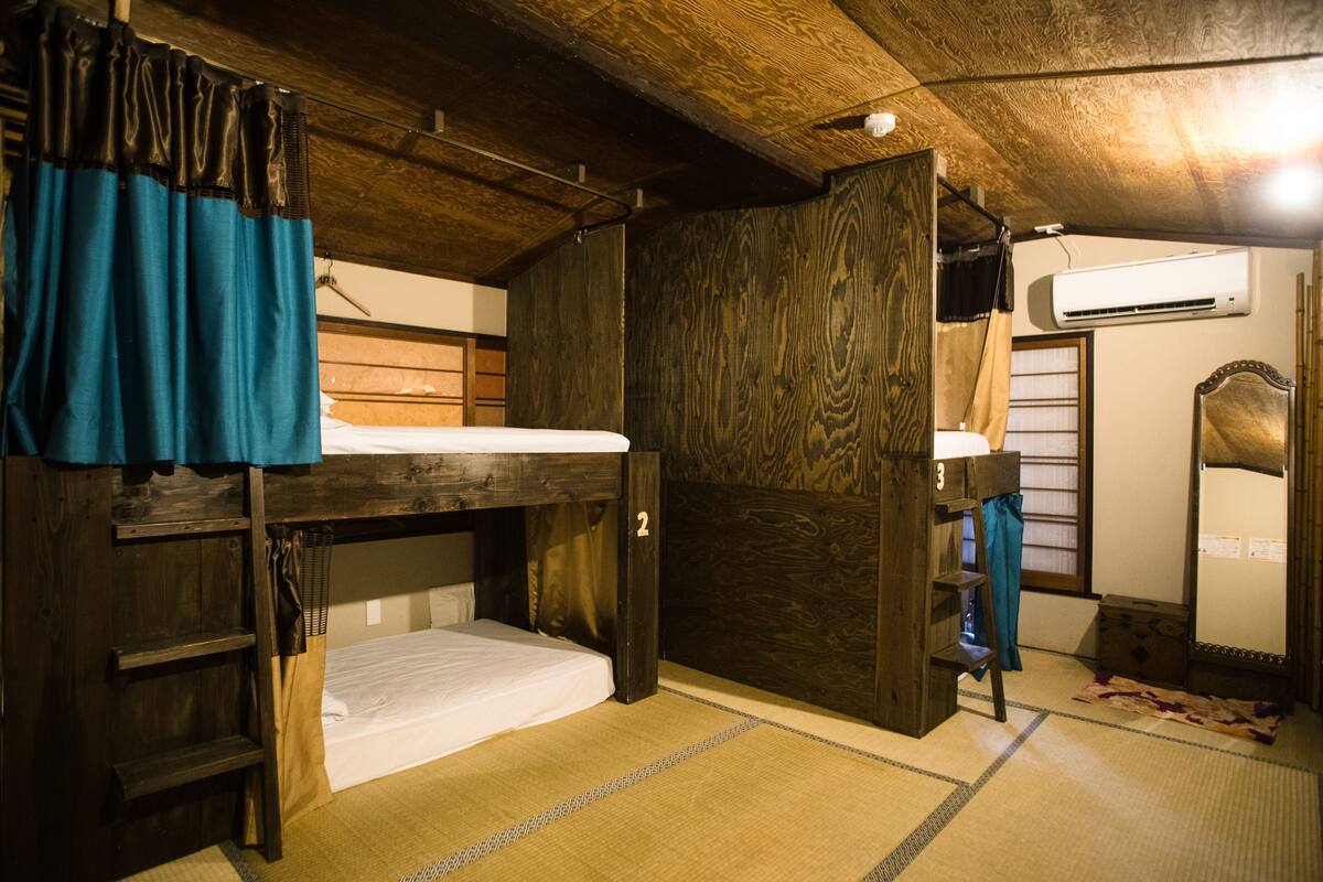 Una habitación con literas, un armario de madera, un estante pequeño y suelo con tatami japonés tradicional.