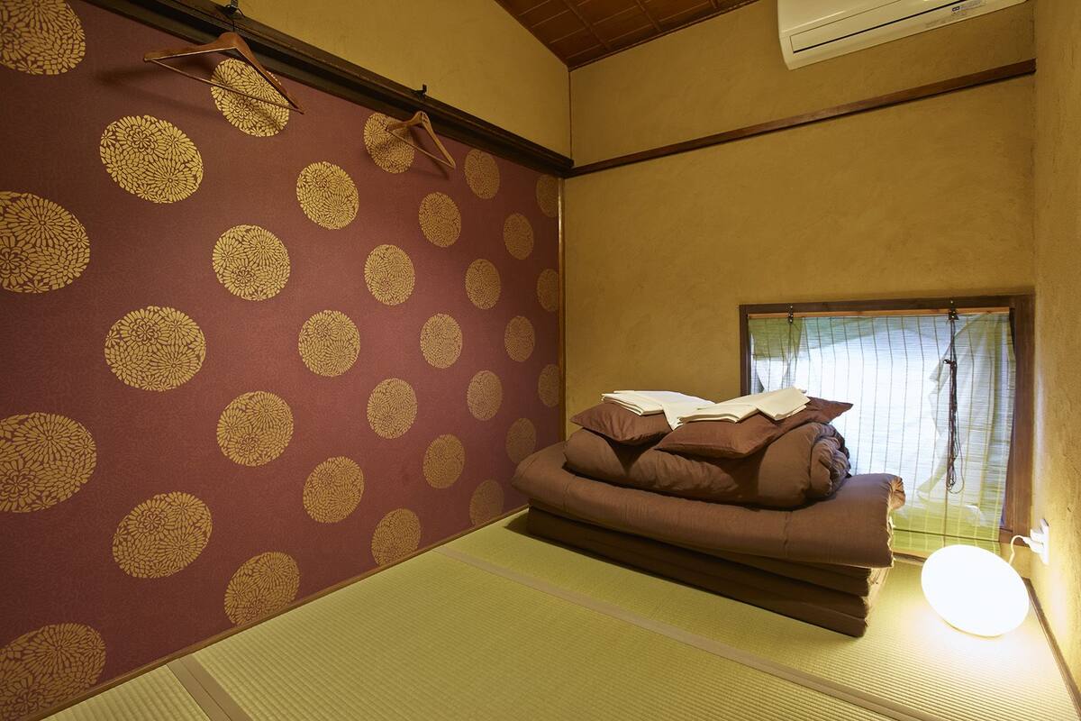 Una habitación con suelo de esteras de tatami, una cama futón, un biombos shoji y un perchero de madera colgante.