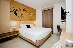 A hotel room with a large bed, a desk with a chair, a television, and a wall with a zodiac sign and quote.